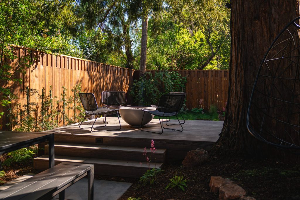 Landscape Design by Seed Studio of Raised Wood Patio with Firepit under a Mature Redwood
