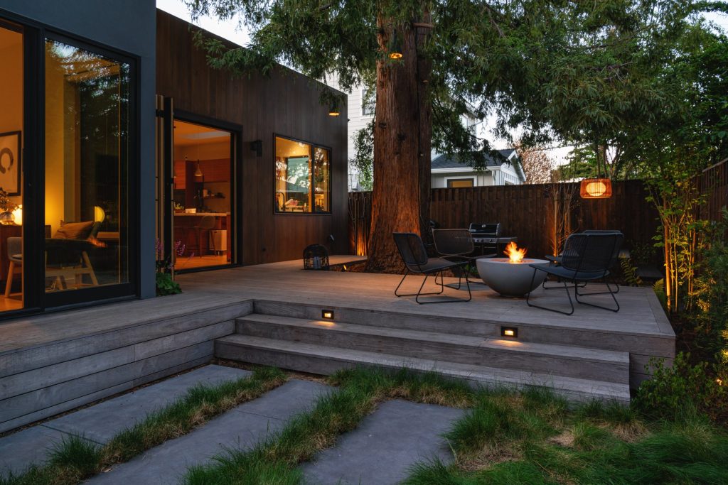 Landscape Design by Seed Studio showing raised wood deck near living room with nearby firepit under mature redwood tree.