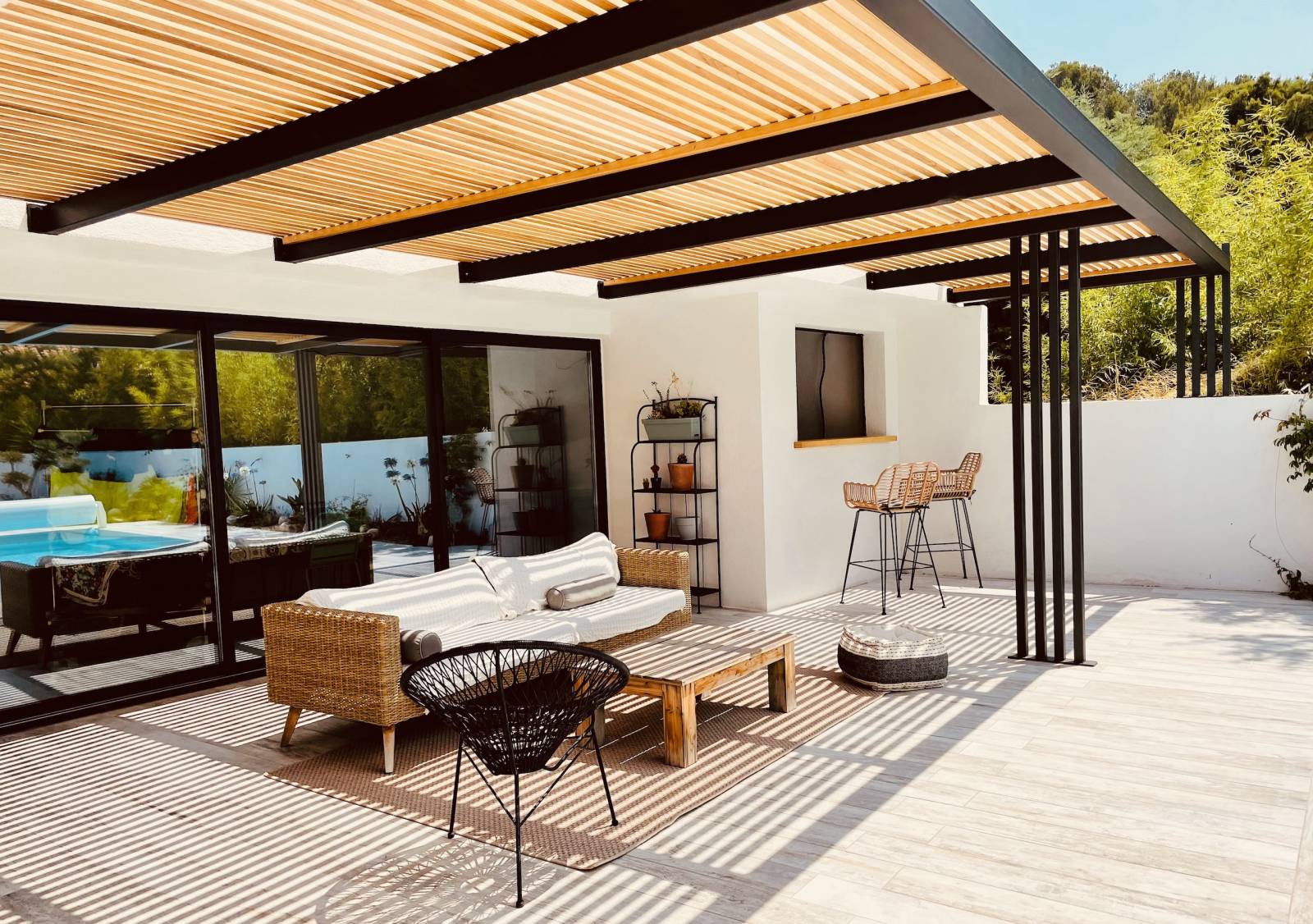 Image of a backyard patio with a pergola covering an outdoor couch offering an indoor and outdoor space.
