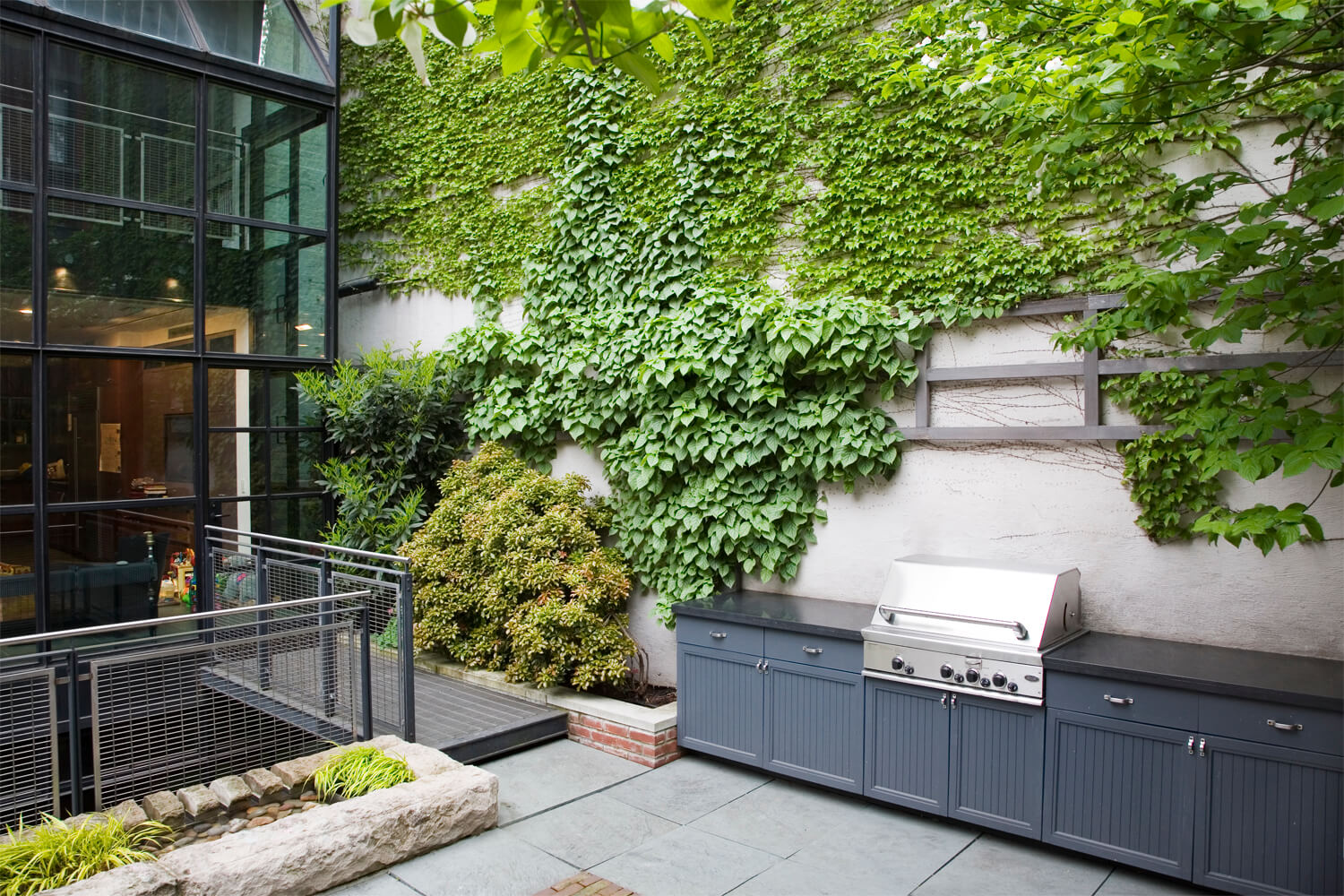 Sunken backyard with an outdoor kitchen and vines growing on a vertical wall in New York by RKLA Studio. Photography by Francine Fleischer.