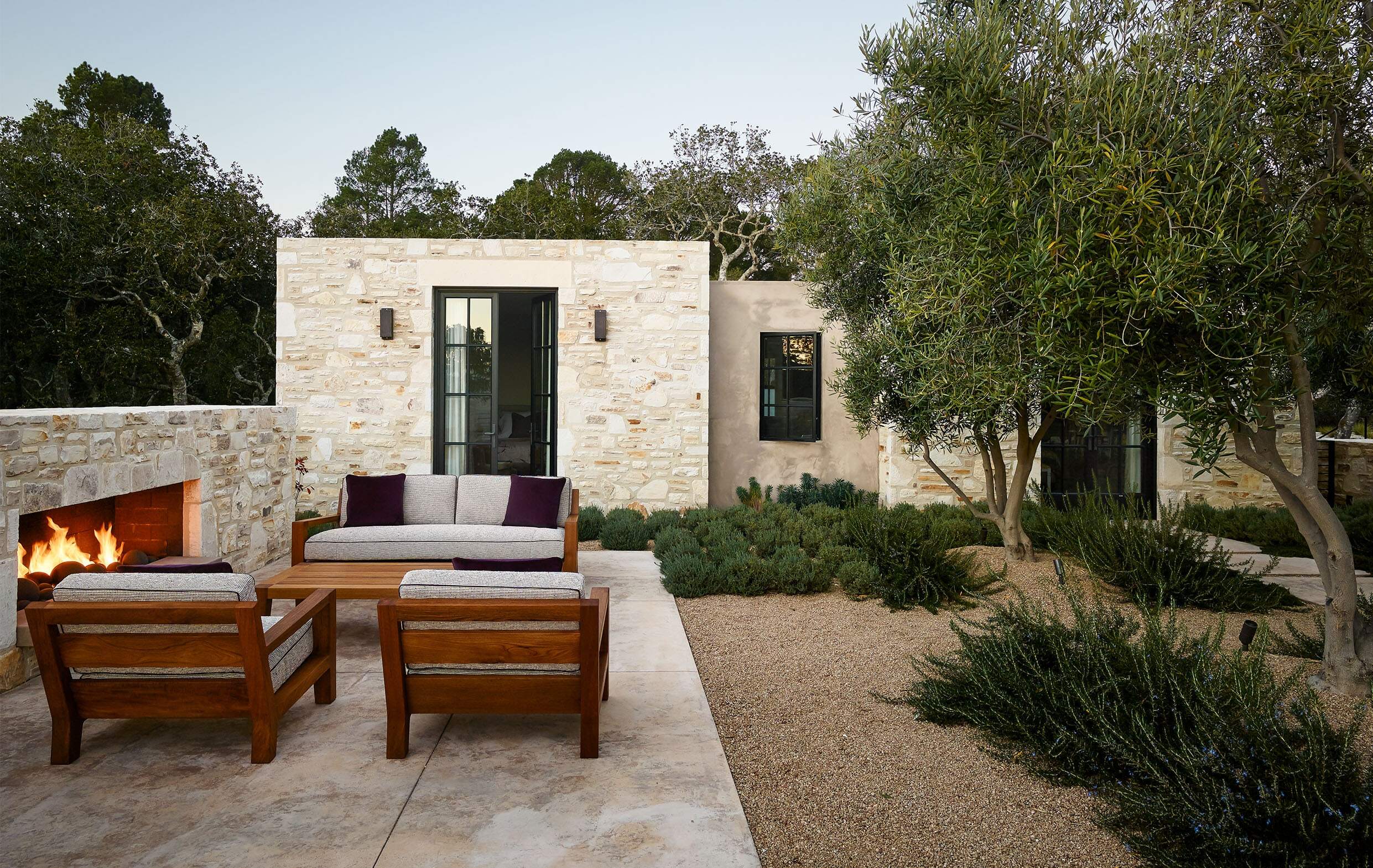 Contemporary natural stone home with a pea gravel patio with irregular plantings dispersed throughout.