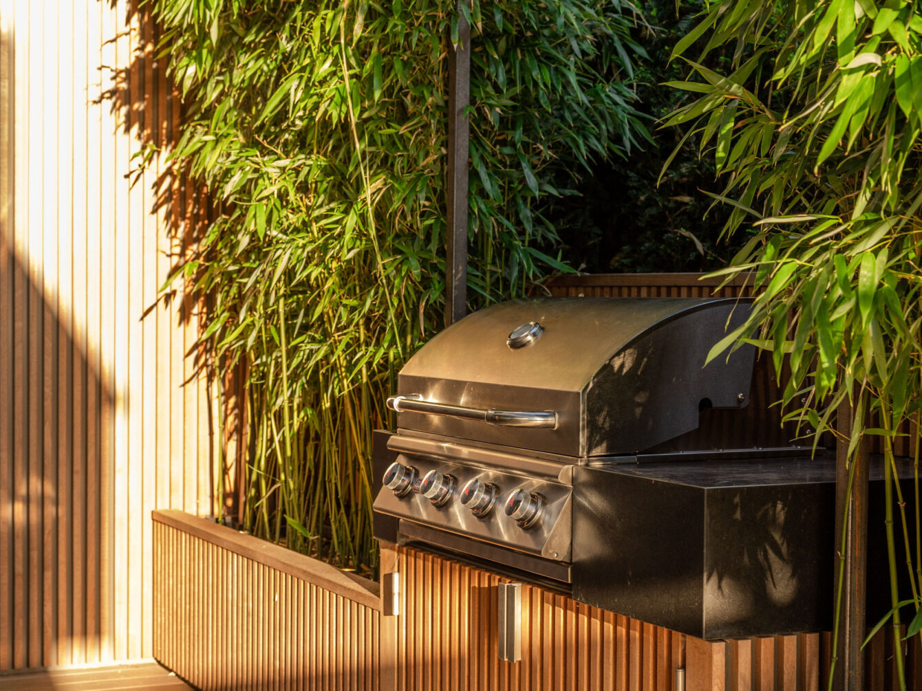 outdoor grill with wood slat base against bamboo landscape screenining.