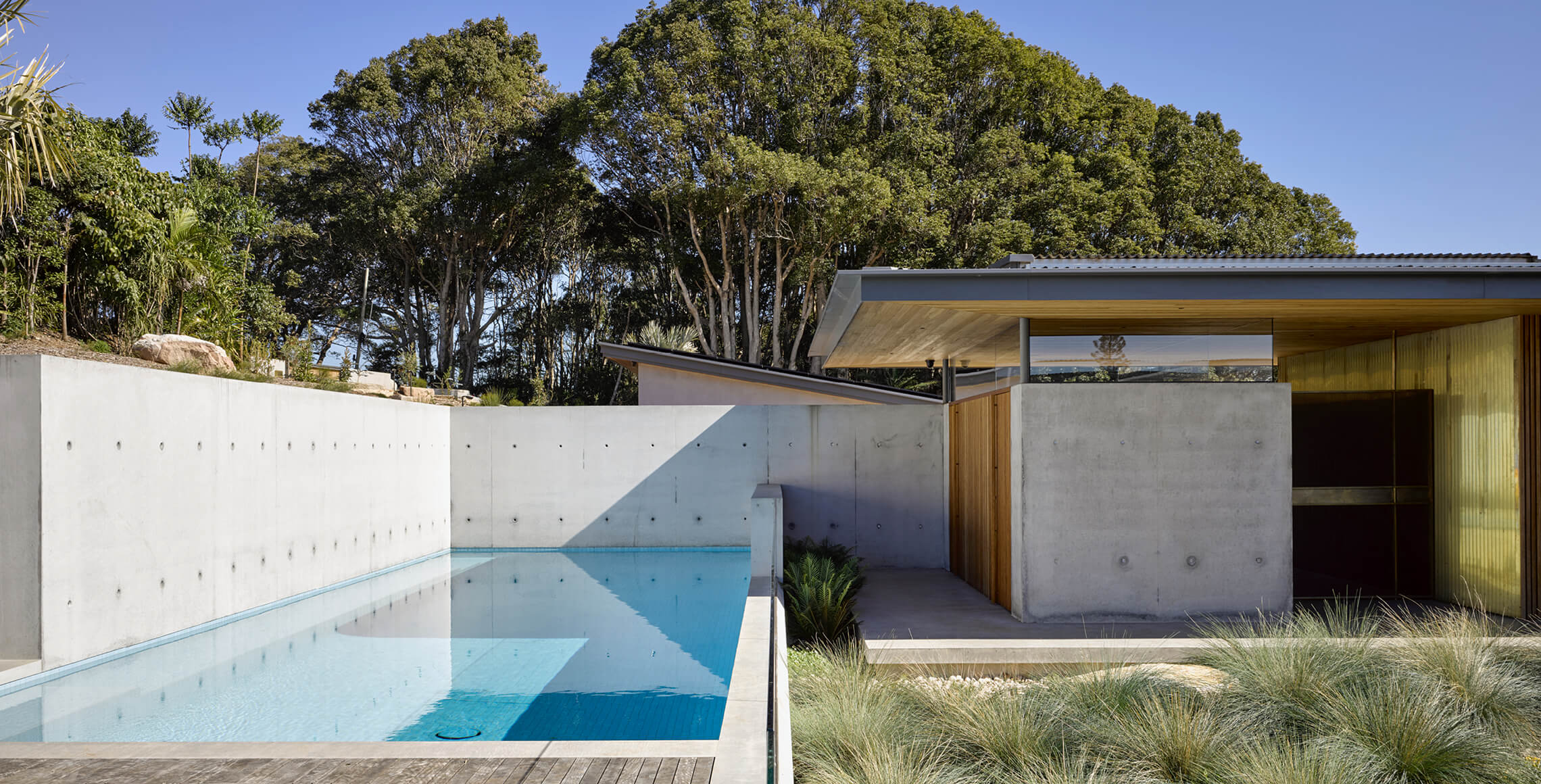 Exposed concrete, brass and wood are key materials for this project and frame views to an in-ground swimming pool.