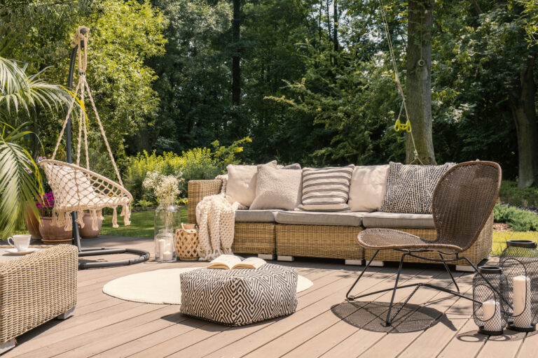 Outdoor furniture pouf and rattan chair on wooden patio with settee in the garden during summer. Real photo