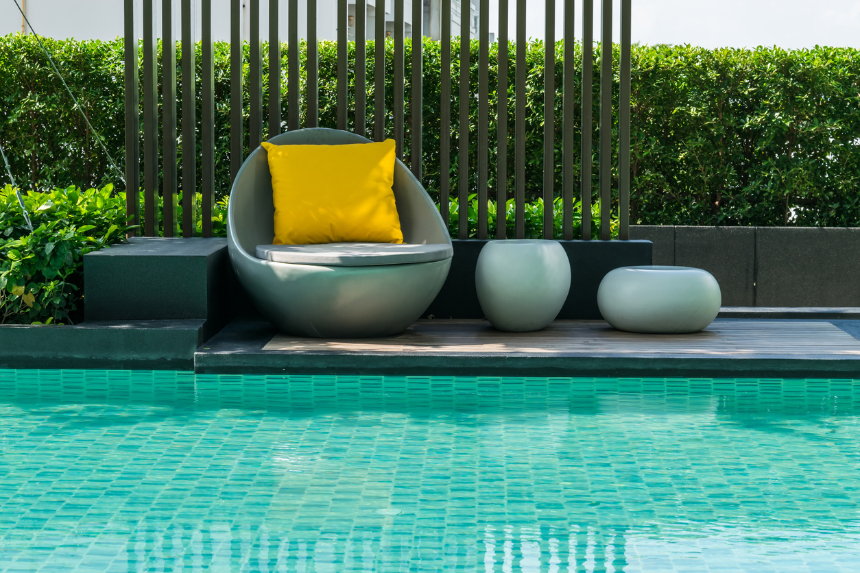 Relaxing outdoor furniture chairs with pillows beside swimming pool.
